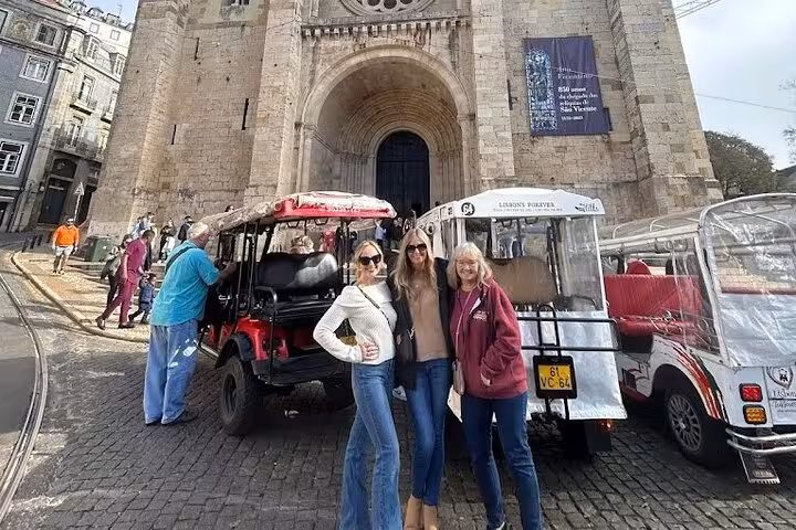 Guests pose by tuk-tuks at Lisbon Cathedral on a 2-hour tuk-tuk city tour before sunset sailing