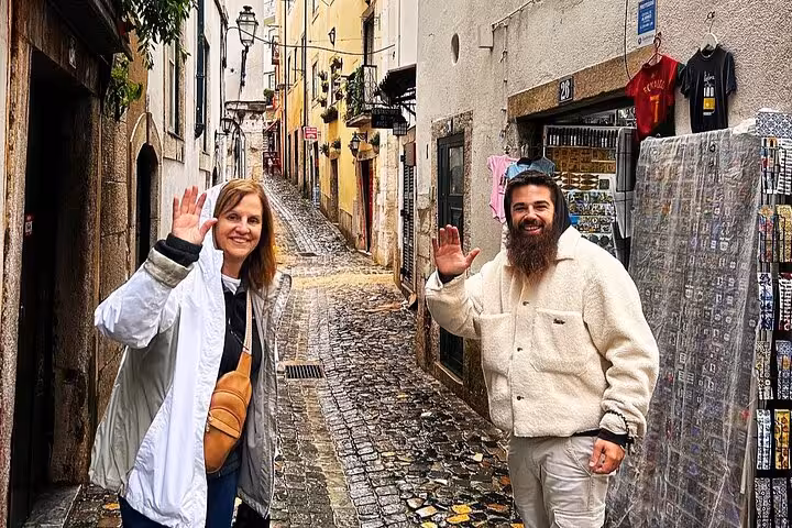 Guide and guests wave in a narrow Alfama alley, a highlight of the 2-hour private Lisbon tuk tuk tour