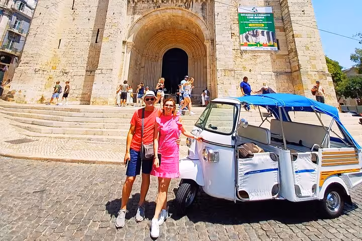 Couple posing by tuk tuk outside Lisbon Cathedral on 1-hour Old Town tuk tuk tour through Alfama highlights