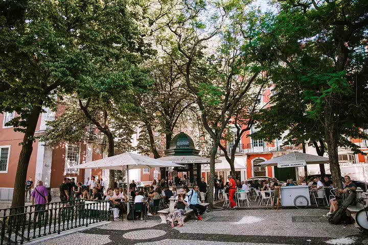 Charming Lisbon square with outdoor café and lush trees, perfect stop on a 4-hour private tuk tuk tour with locals.