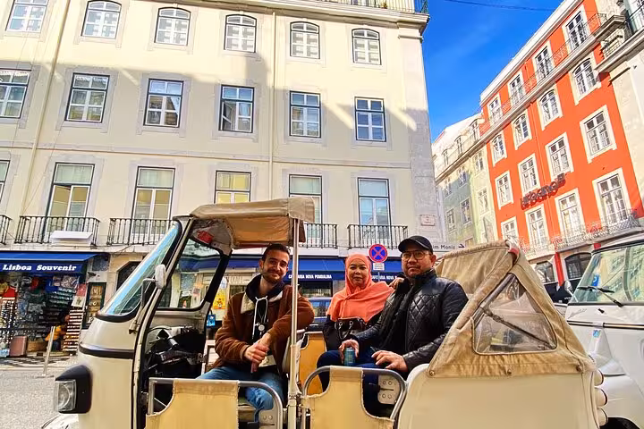 Happy travelers in a tuk tuk on Lisbon Old Town tour, passing colorful Baixa buildings on a sunny day