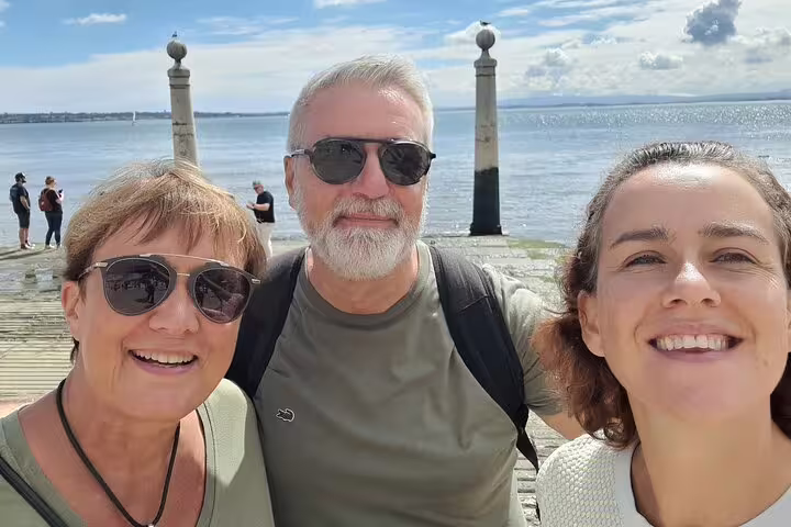 Group of tourists smiling by the Tagus River in Lisbon, highlighting the scenic stops on a walking tour.
