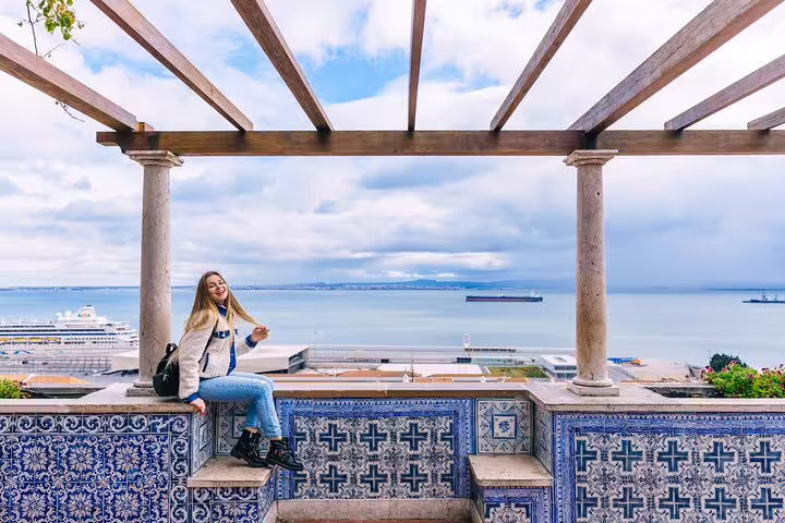 Woman enjoying scenic view from Lisbon terrace with traditional azulejos tiles, overlooking the Tagus River and cruise ships.
