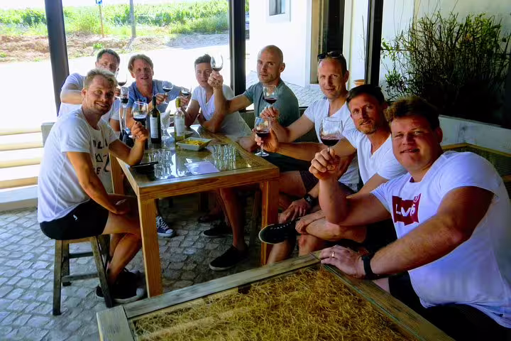 Group enjoying wine tasting at a rustic Lisbon winery, part of the Lisbon Surf & Wine tour, featuring scenic vineyard views.