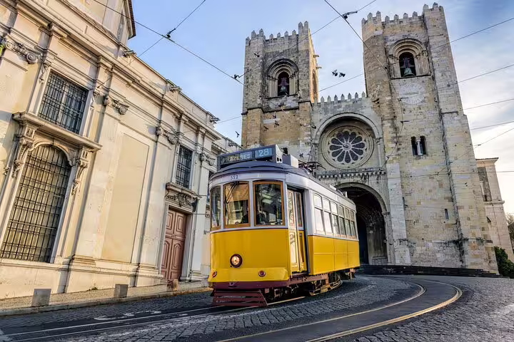 Yellow tram passes Lisbon Cathedral on a sunny day, highlighting the charm of a full-day private tour and gastro experience.