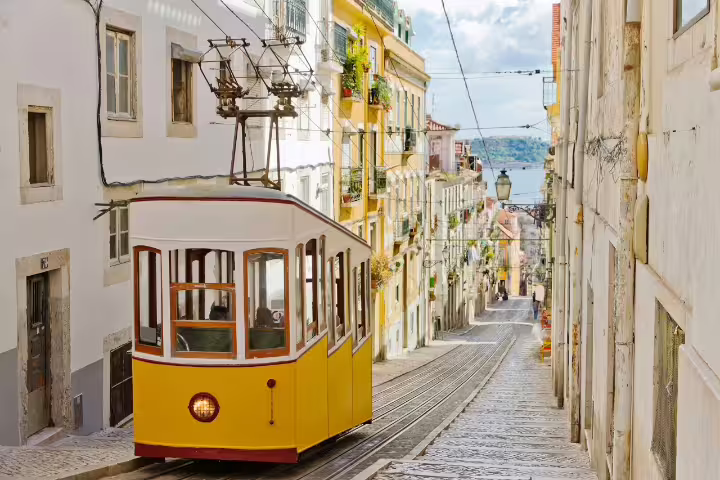 Historic yellow tram navigating the charming cobblestone streets of Lisbon, showcasing vibrant architecture and scenic city views.
