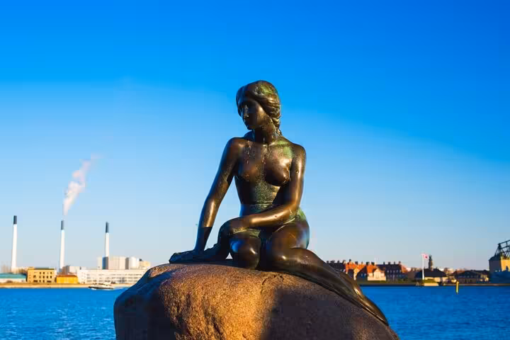Bronze Little Mermaid statue perched on a rock in Copenhagen harbor on a sunny day