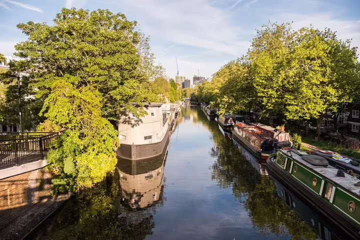 Narrowboats moored along a calm tree-lined canal in Little Venice, London on a sunny day