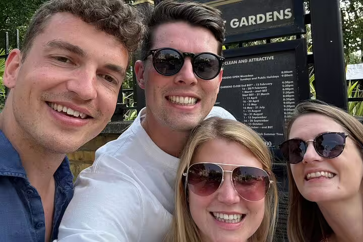 Four smiling friends taking a selfie at London Gardens entrance on a sunny day