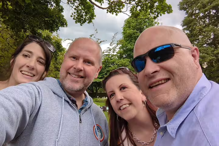 Four smiling adults taking a selfie outdoors in a lush green park in London