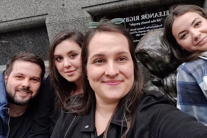 Four smiling visitors posing for selfie at Eleanor Rigby statue in Liverpool