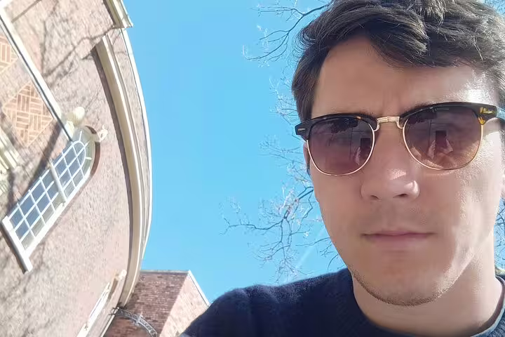 Man wearing sunglasses taking a selfie outside a historic brick building in Liverpool on a sunny day