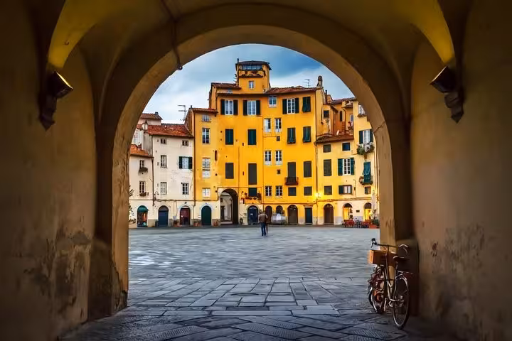 Picturesque archway view of Piazza dell'Anfiteatro in Lucca, highlighting vibrant buildings on a Livorno excursion.