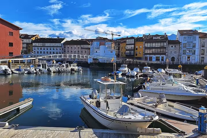 Scenic view of Llanes harbor with moored boats and colorful buildings, perfect for exploring Asturias' coastal charm.