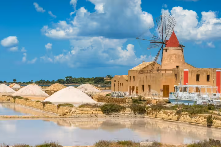 Historic windmill and white salt piles reflected in the Lo Stagnone saltpans near Mothia Island on a private tour from Palermo