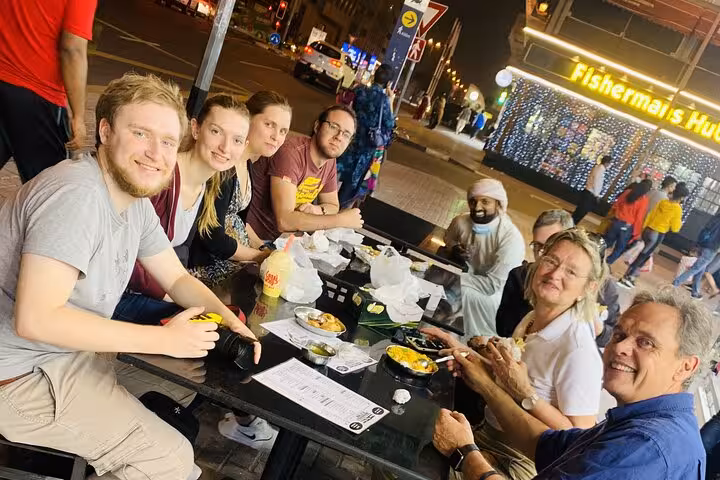 Group sharing local food tastings outdoors on Old Dubai walking tour, shopping in souks and abra boat ride
