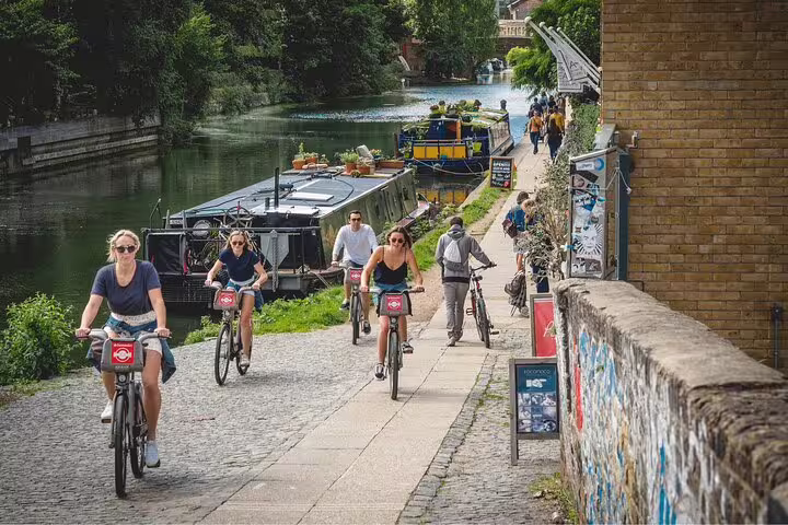 Cyclists enjoy a scenic London bike tour along the canal, passing colorful houseboats and vibrant street art.
