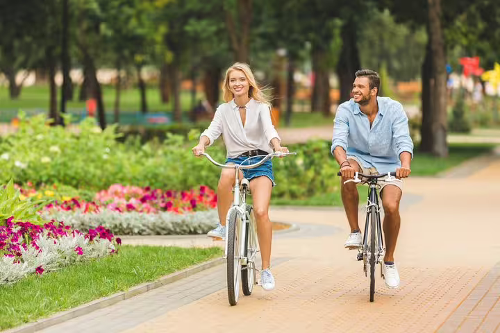 Couple enjoying a scenic London bike tour on a sunny day, exploring city highlights with vibrant gardens in the background.