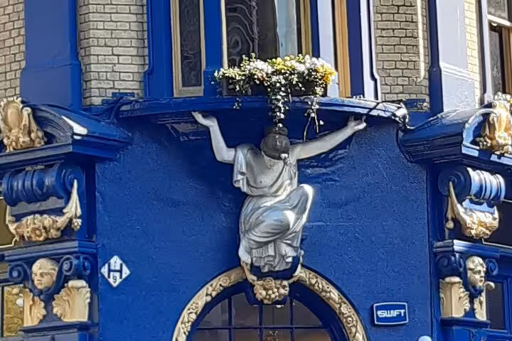 Silver caryatid statue supporting a flower-filled balcony on a vibrant blue ornate building facade in London