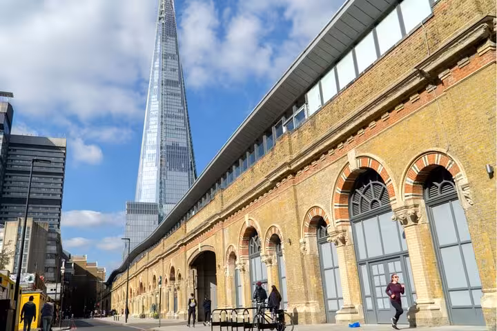 The Shard skyscraper towering above Victorian brick arches near London Bridge on a sunny day