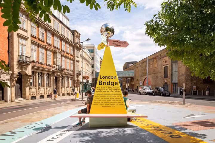 Yellow London Bridge monument sign with directional arrows and mirrored sphere on a sunny Southwark street