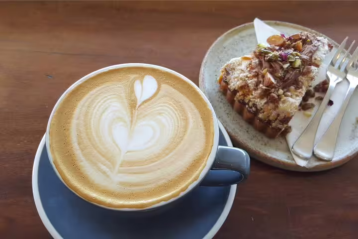 Latte with heart art and a slice of nut-topped cake on a plate, showcasing a taste of London's vibrant café culture.