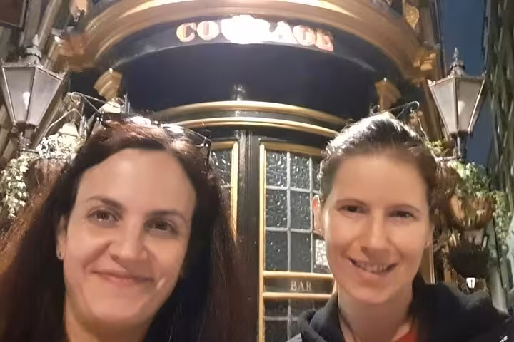 Two women smiling in front of Courage pub bar during London walking tour at night