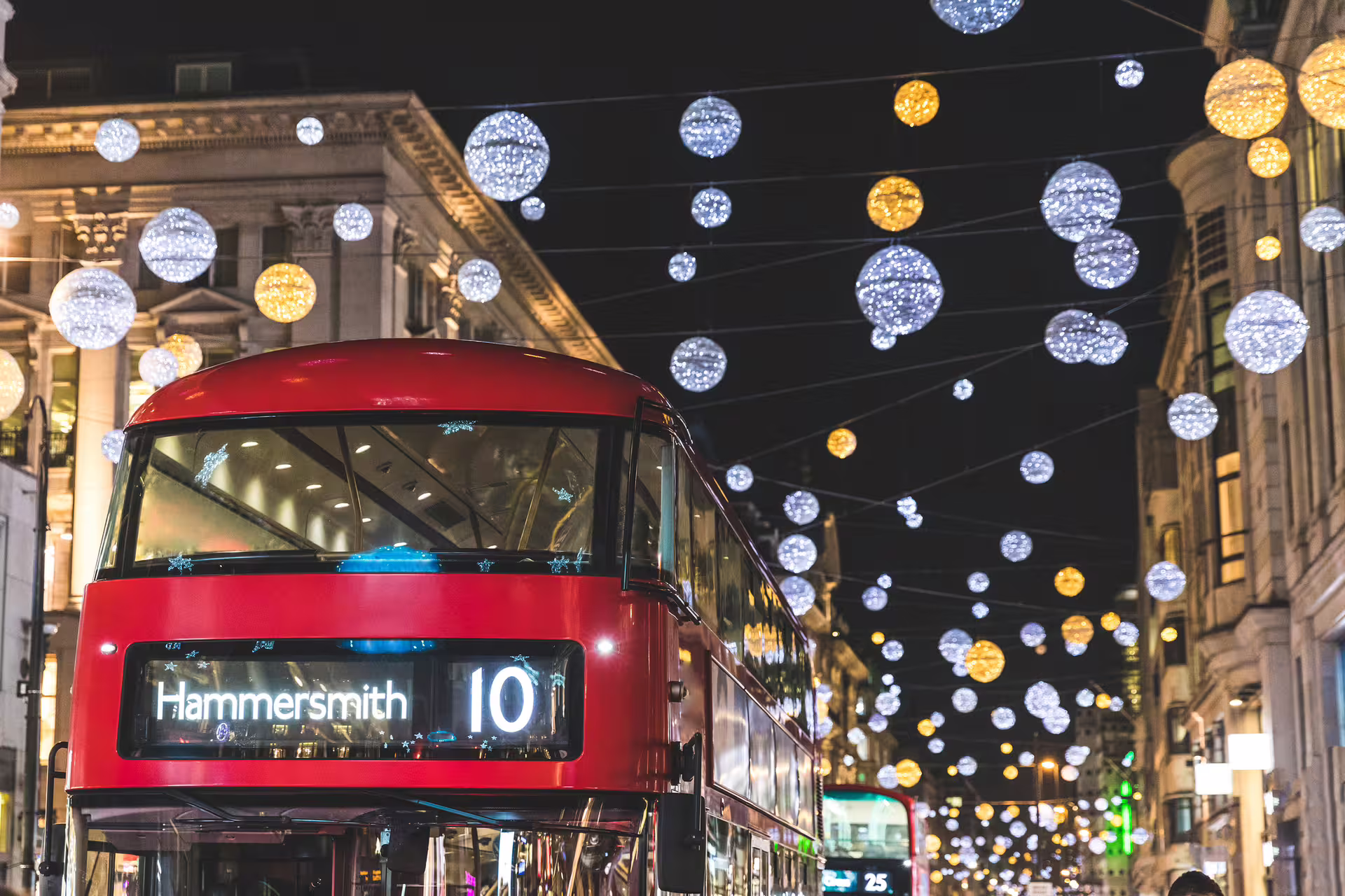 Red London double-decker bus under festive West End lights near Covent Garden, perfect for 1-day audio tour