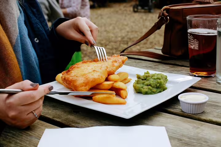 Person enjoying traditional fish and chips with mushy peas and a drink during London private tour near Westminster Abbey.