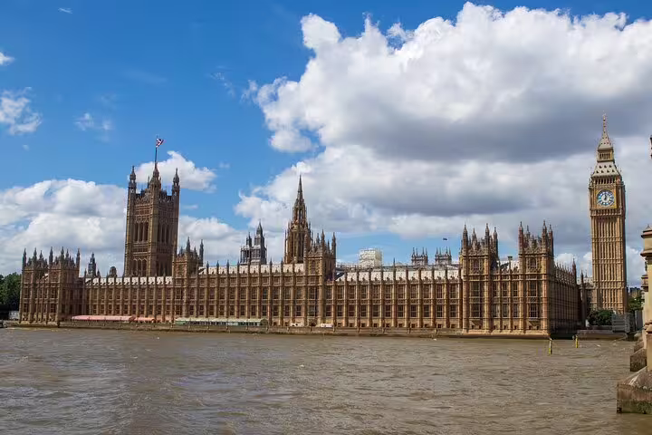The iconic Houses of Parliament and Big Ben under a blue sky, viewed from across the River Thames in London.