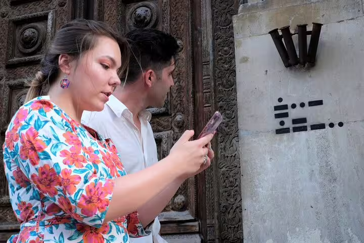 Two people examining morse code clues on a stone wall during a London walking escape game tour