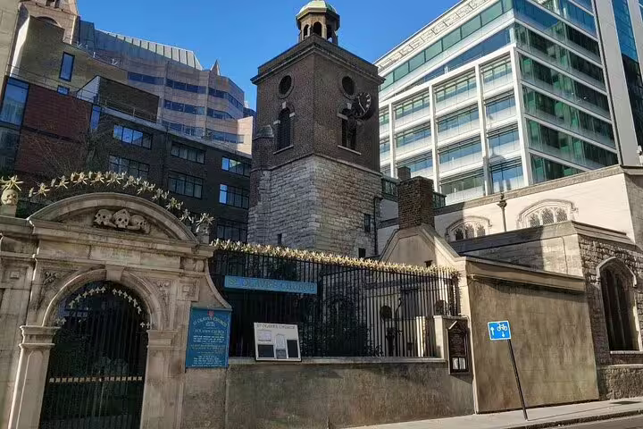 Historic London church tower surrounded by modern buildings, iron gate with blue information sign