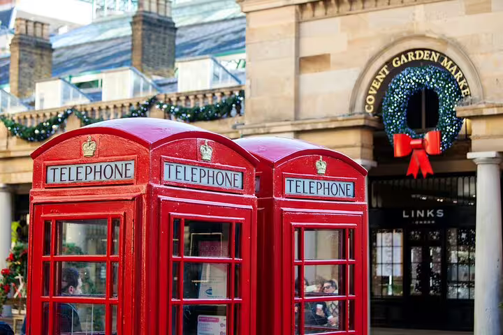 Red telephone boxes in front of Covent Garden Market, London, decorated for the holidays, highlight a classic city tour stop.