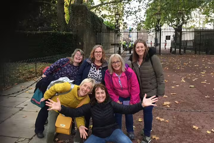Group of six women posing and laughing outdoors near iron gates and autumn trees in London