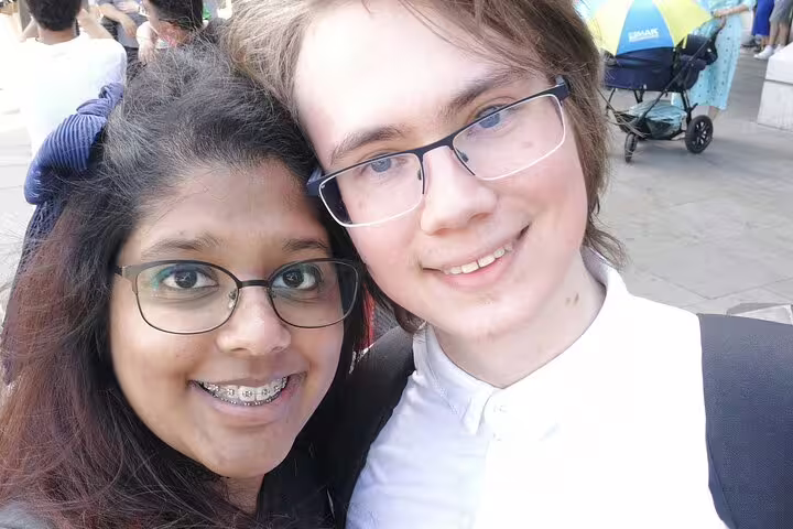 Two smiling teens wearing glasses take a selfie outdoors in London on a sunny day