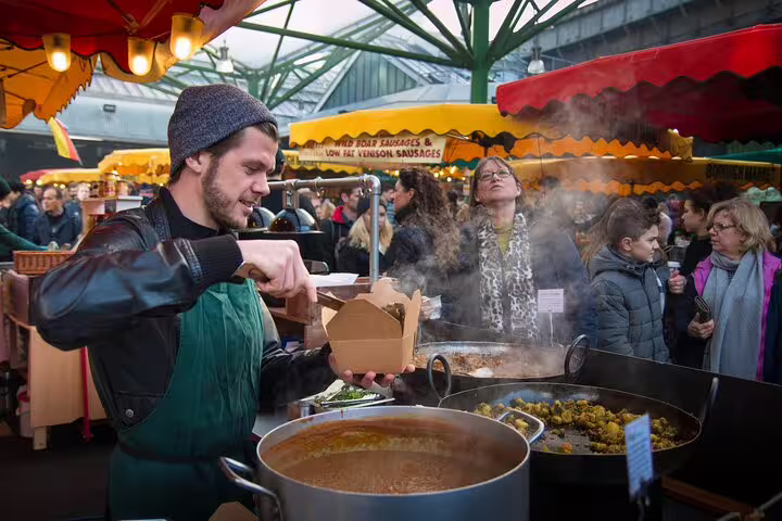 Man serving street food at bustling London market during private city tour, highlighting local culture and culinary delights.