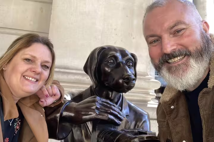 Two smiling tourists posing with a bronze dog statue during a self-guided walking tour in London