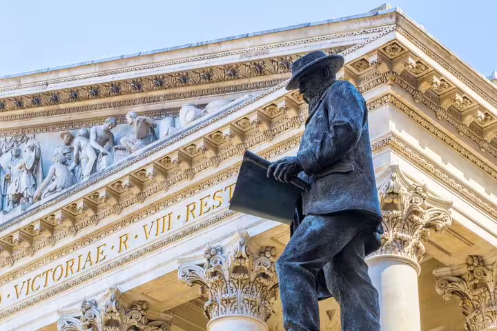 Bronze statue of a man holding a book outside a neoclassical building with Latin inscription in London