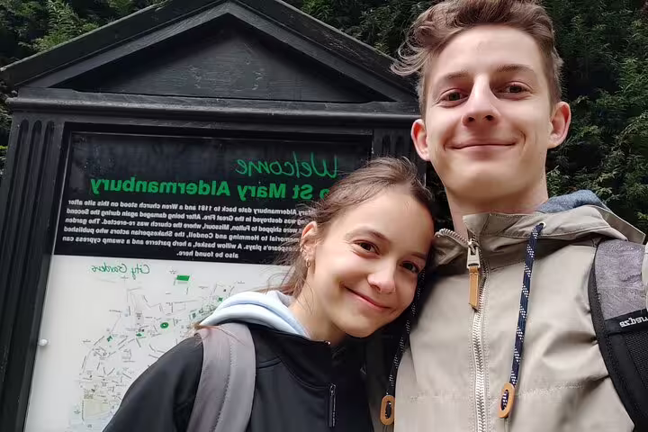 Two young tourists smiling in front of St Mary Aldermanbury sign during London walking tour