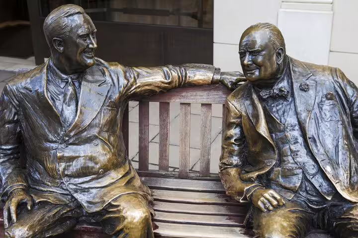 Bronze statues of two men in suits seated on a bench in London