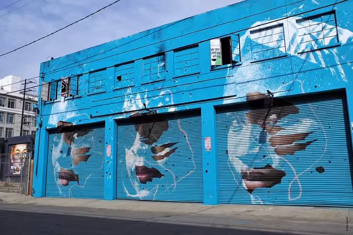 Vibrant turquoise building with large street art mural of faces on garage doors in Los Angeles