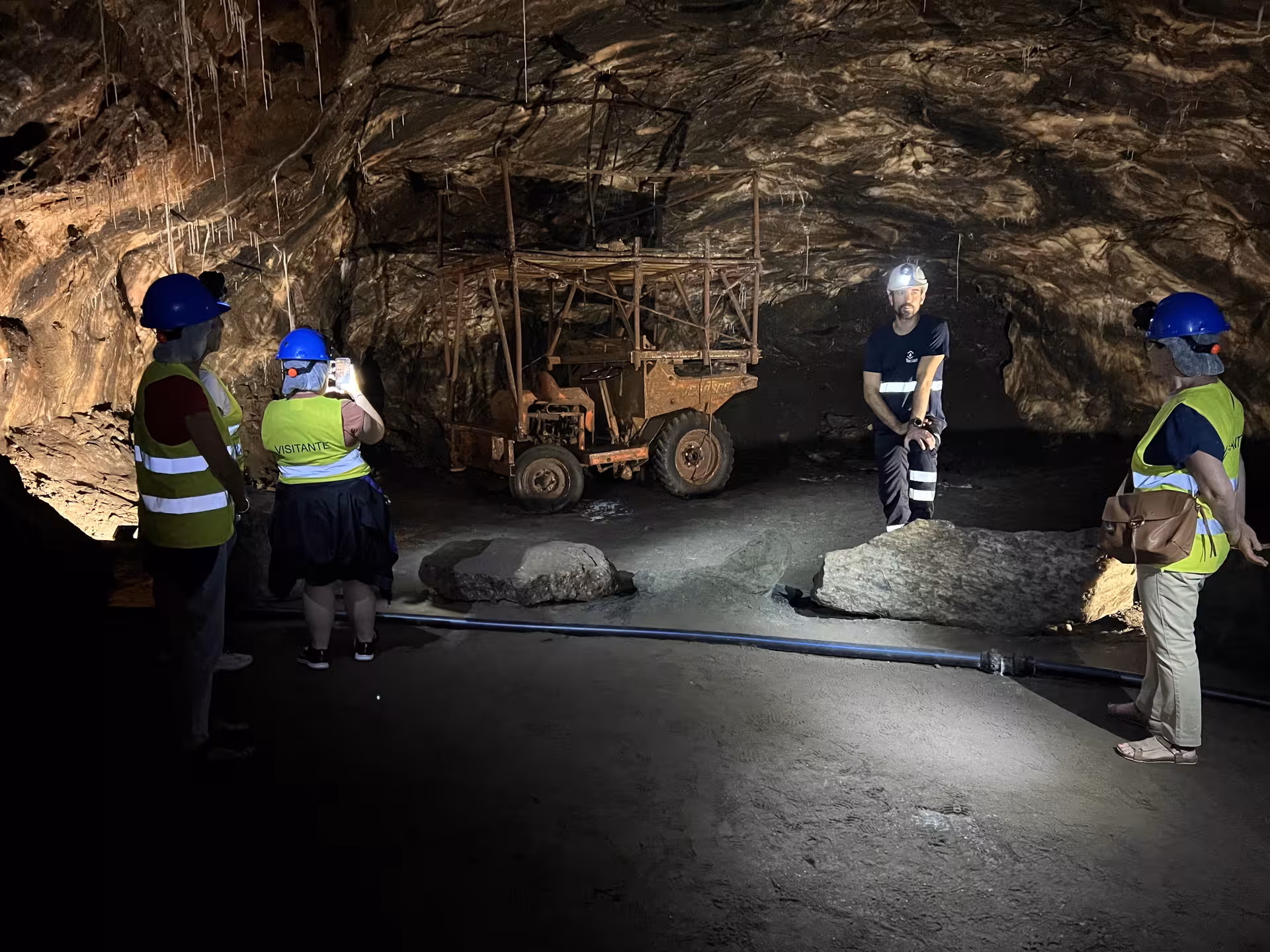 Tourists explore the illuminated interior of Loulé rocksalt mine, guided by an expert in a helmet.
