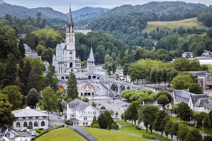 Aerial view of Lourdes showcasing the stunning Basilica of Our Lady amidst lush greenery, ideal for a guided city walk.