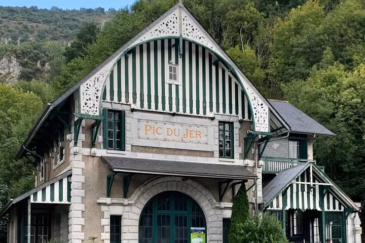 Historic Pic du Jer funicular station in Lourdes, nestled among lush trees and hills, a highlight of the city walk.