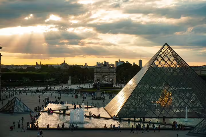 Louvre Museum glass pyramids with fountains and Arc de Triomphe du Carrousel at sunset in Paris