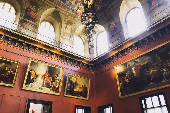 Ornate red-walled Louvre gallery hall with classical paintings and arched windows on upper level