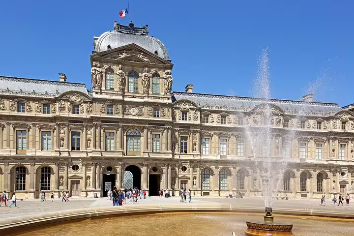 Louvre Museum courtyard with ornate French baroque facade, fountain, and visitors on a sunny day in Paris