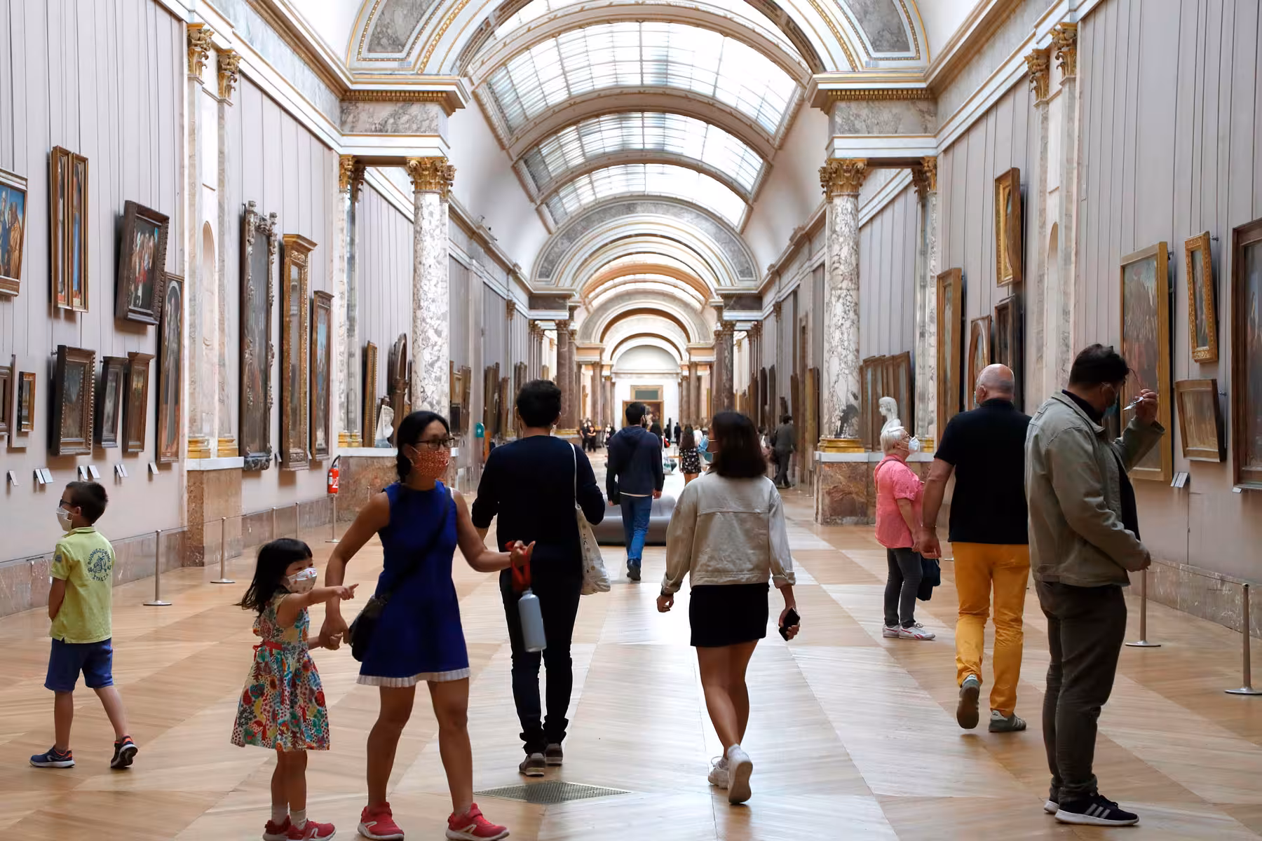 Visitors exploring a grand painting gallery at the Louvre Museum in Paris