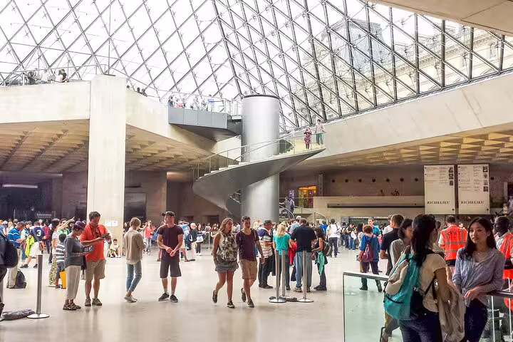 Busy Louvre Museum entrance hall under iconic glass pyramid with tourists exploring the lobby