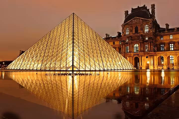 Louvre Museum glass pyramid illuminated at night with golden reflections in Paris